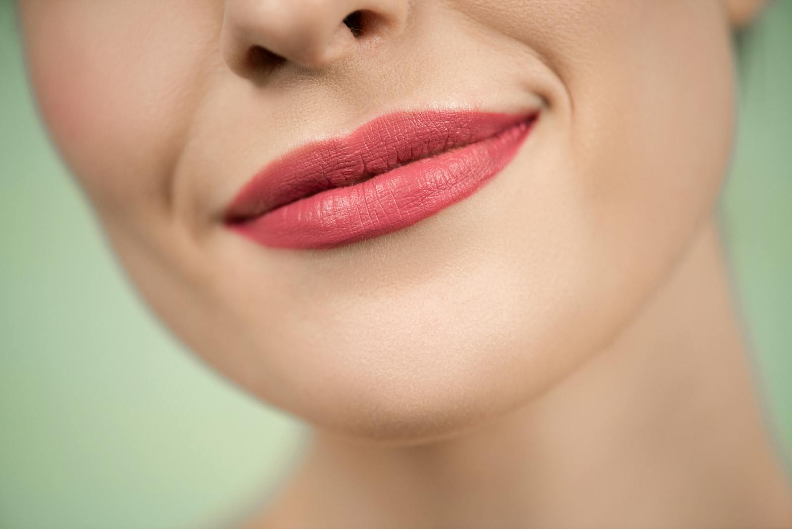 A detailed close-up of a woman's smile with pink lipstick on a green background.